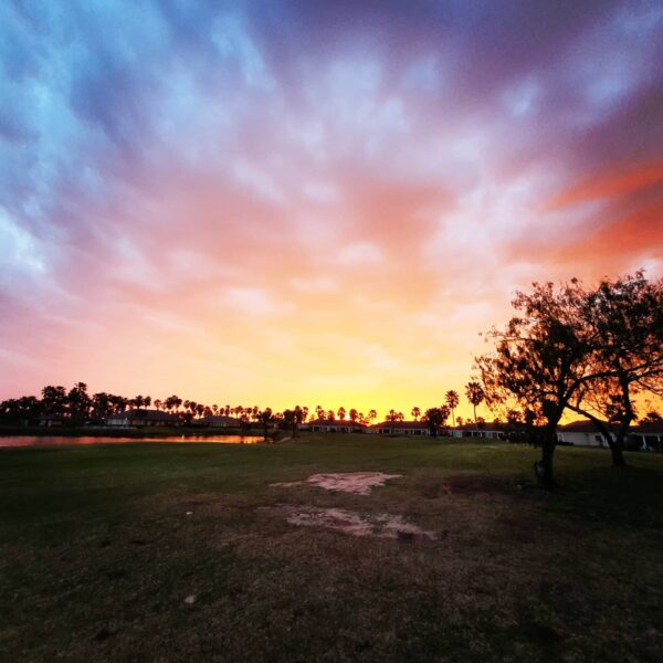 Sunrise over South Padre Island Golf Club illuminating clouds in the sky and showcasing homes behind the green.